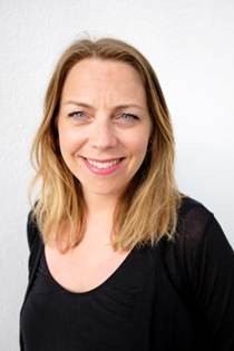 A female academic with mid length straight light brown hair, smiling wearing black top
